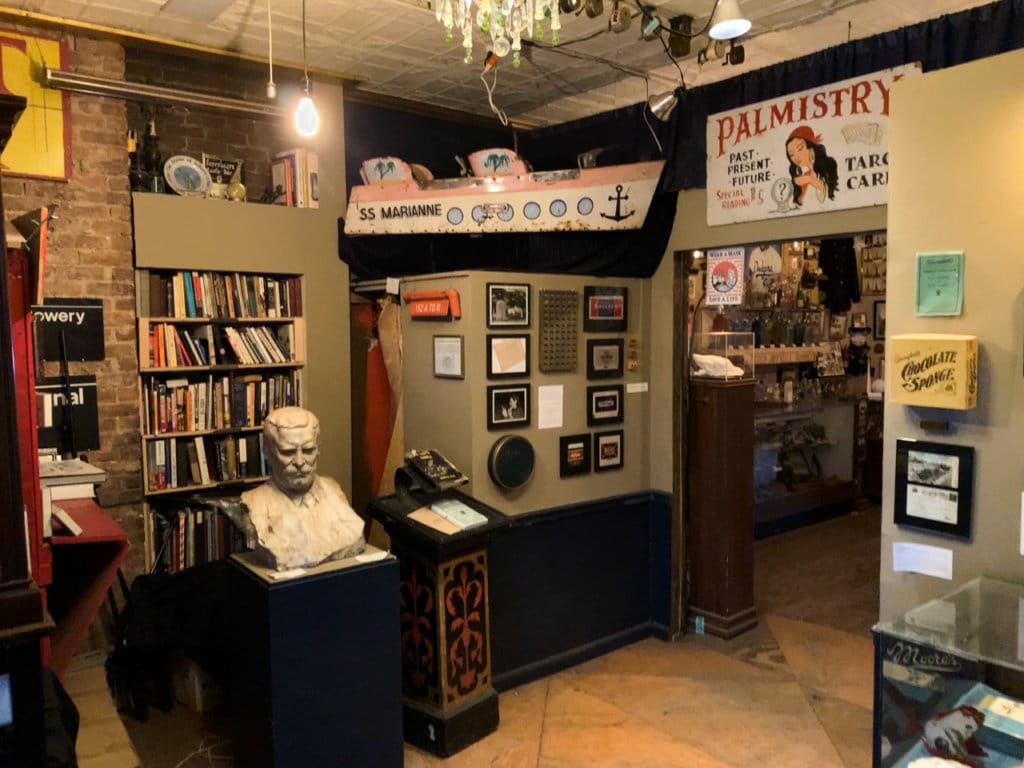 Gallery in a small museum filled with random items such as a bust of T. Roosevelt and a palm-reading sign.
