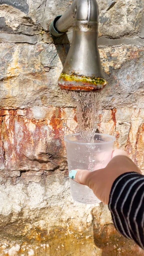 A hand holding a cup under a stream of water at a Saratoga mineral spring.