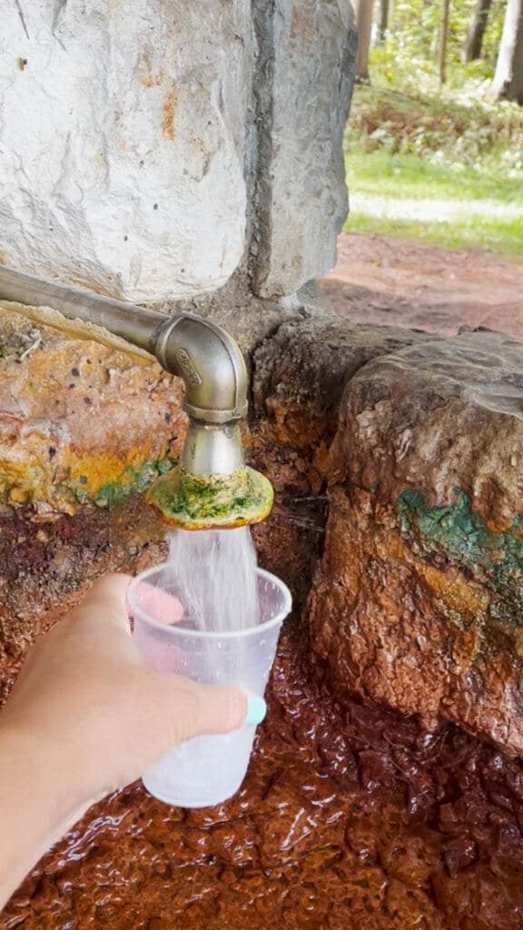 A hand holding a cup under a flow of water at a Saratoga mineral spring.