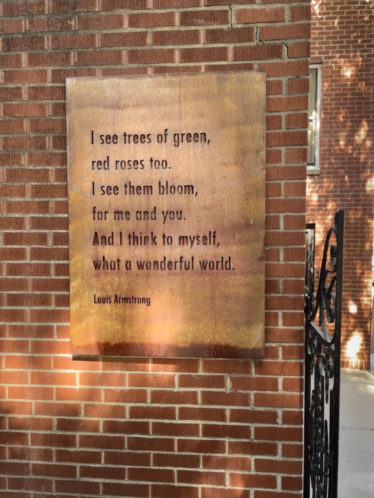 Metal plaque on a brick wall with opening lyrics to the song, What a Wonderful World, by Louis Armstrong.