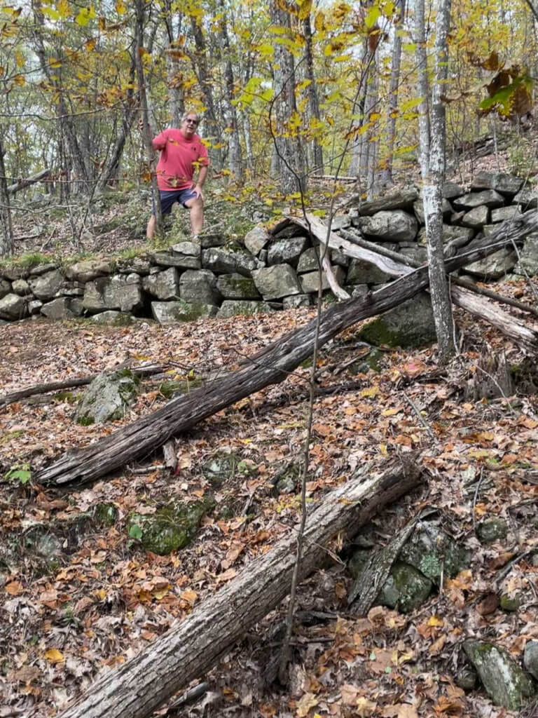 Man on a hiking trail lined with rocky retaining wall. 
