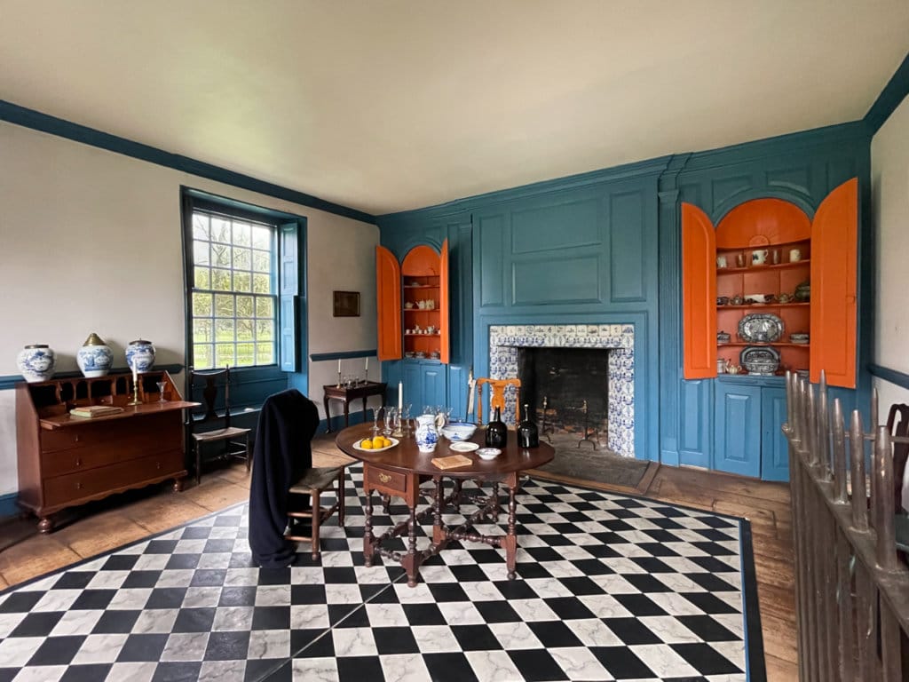 Dining room in a house museum decorated. Floor is black and white checkered. Walls and cupboards are blue and orange.  