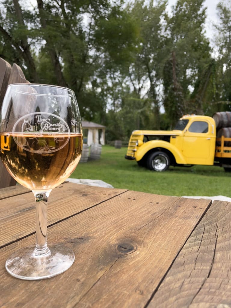Glass of rose sitting on a barrel with an old-fashioned yellow truck in the background.
