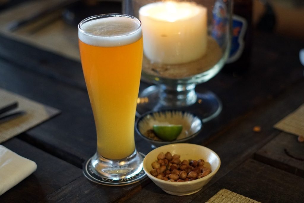 A draft beer, a small bowl of peanuts, and a lit candle. 