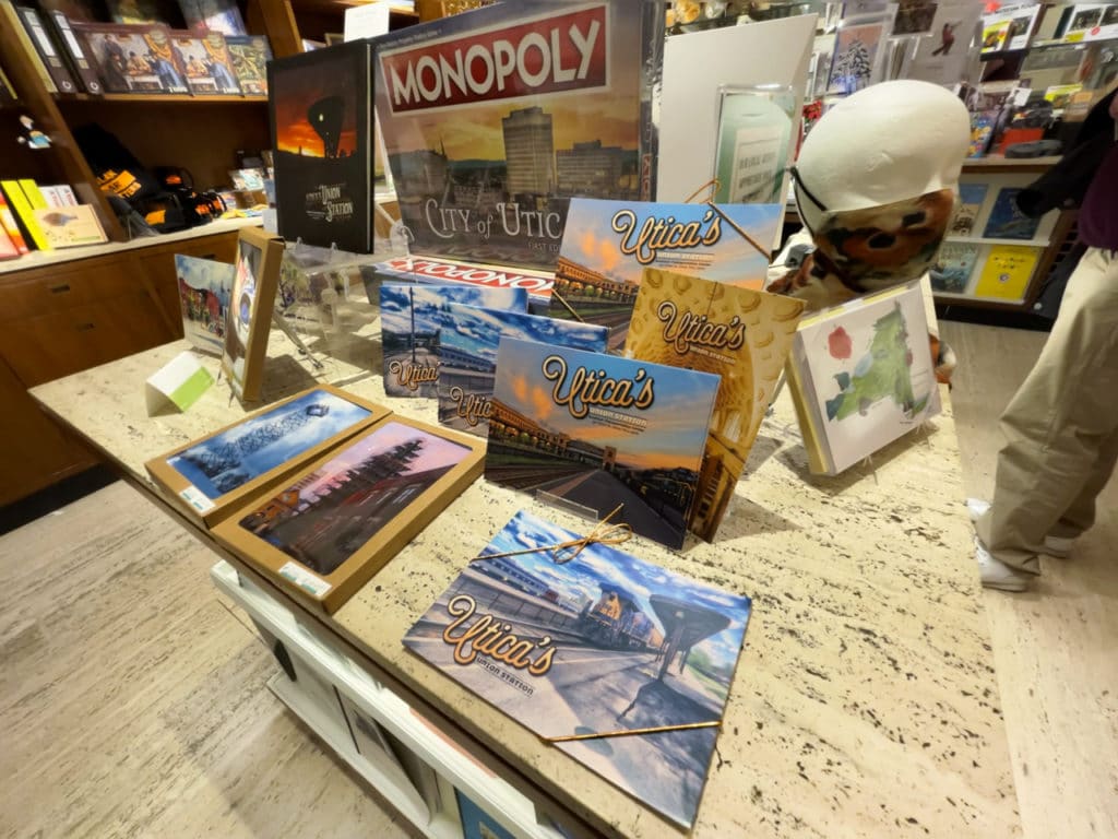 Table in a gift shop with puzzles, framed photographs, and a Monopoly game, all with a Utica, NY theme.