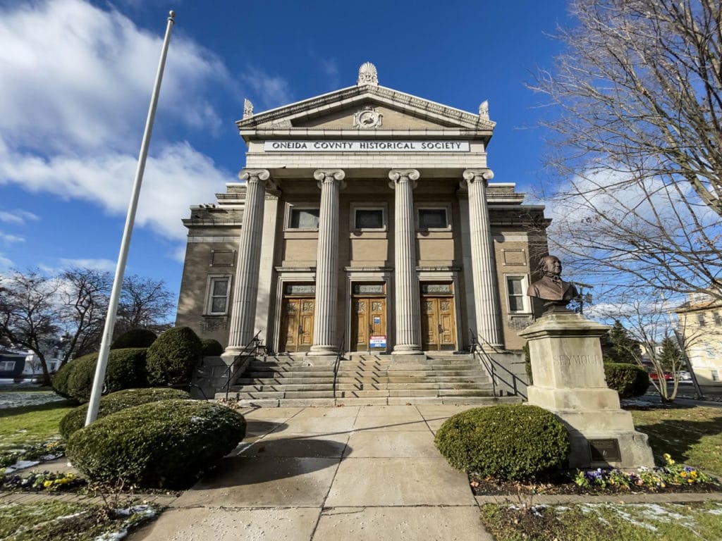Outside Oneida County History Center in Utica, NY, a classical-style building with four large columns leading to the portico.