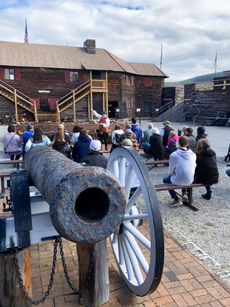 A tour guide wearing a 17th century British military uniform, talking to an audience outside at the Fort William Henry Museum in Lake George, NY.