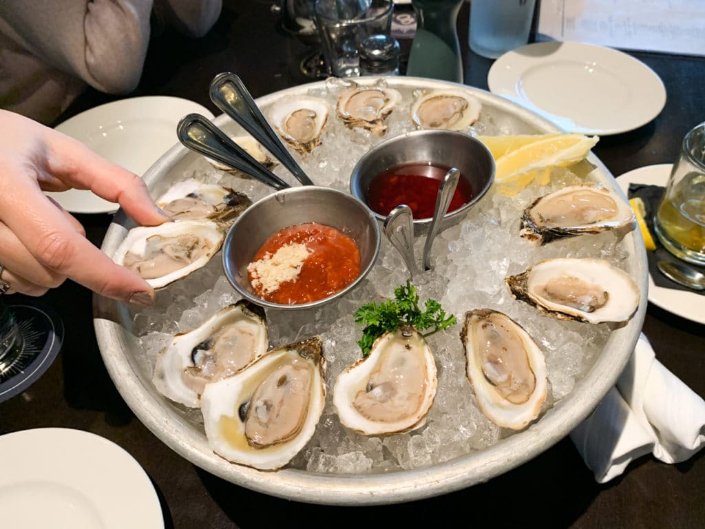A dozen oysters on ice with dipping sauces in the middle.
