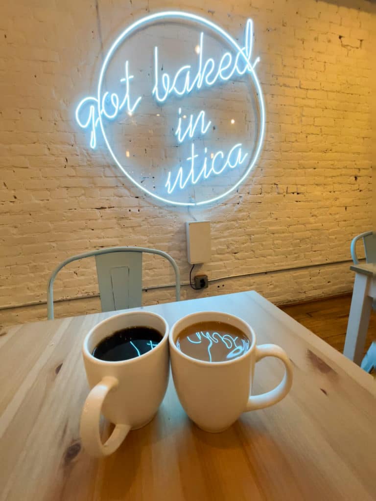 Two cups of coffee below a neon sign that says Got Baked in Utica. At Wisk Baking Co. in Utica, NY.