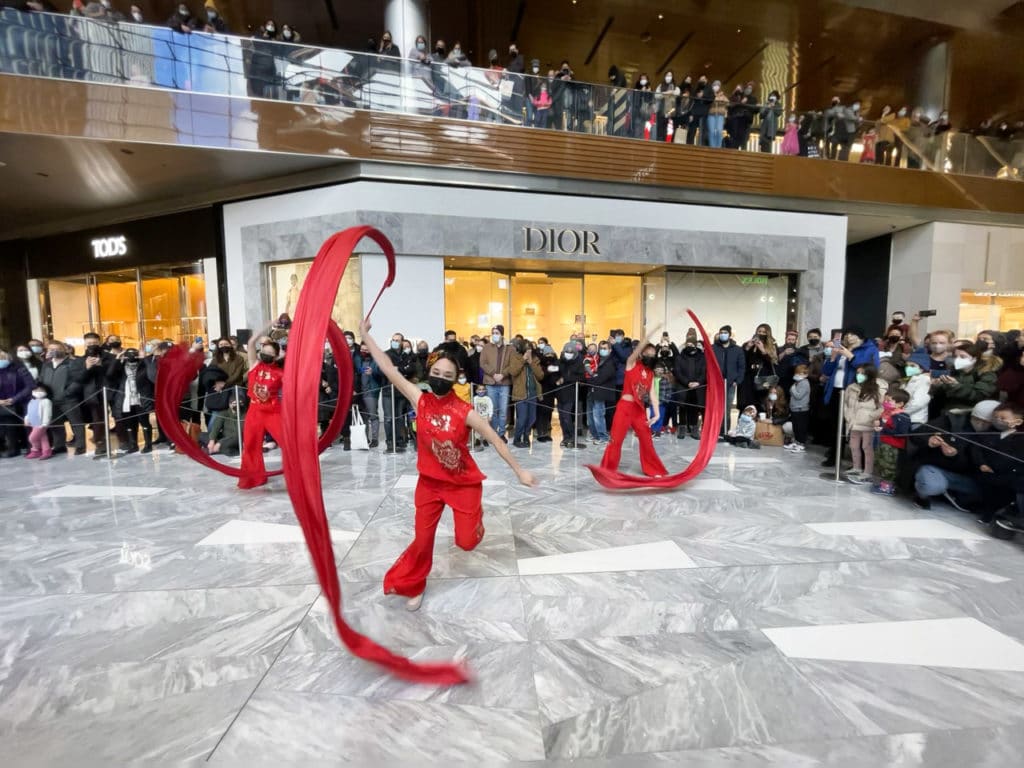Three dancers dressed in red performing a ribbon twirling dance inside the mall at Hudson Yards.
