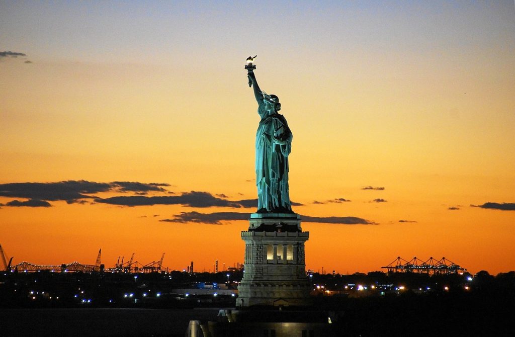 Full view of the Statue of Liberty at sunset. The sky is deep orange and yellow. 