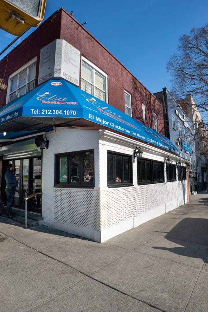 Exterior of a restaurant with a blue awning on a Manhattan street corner. 