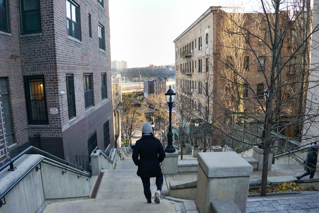 Woman walking down a long concrete staircase in between apartment buildings in Inwood, New York City. 