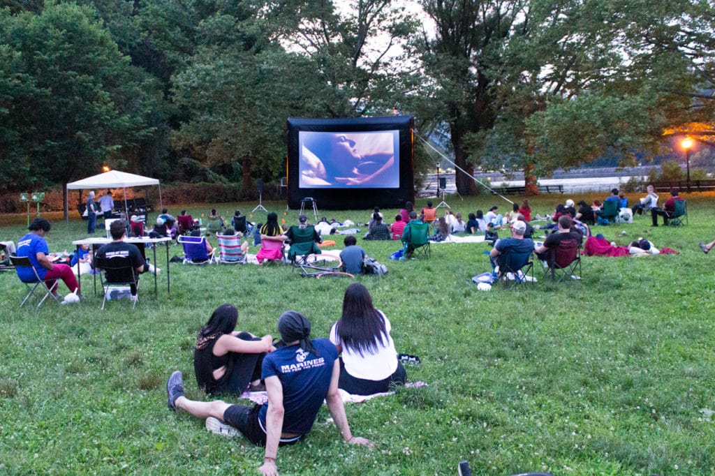 People sitting on a lawn watching an outdoor movie in Inwood Hill Park.