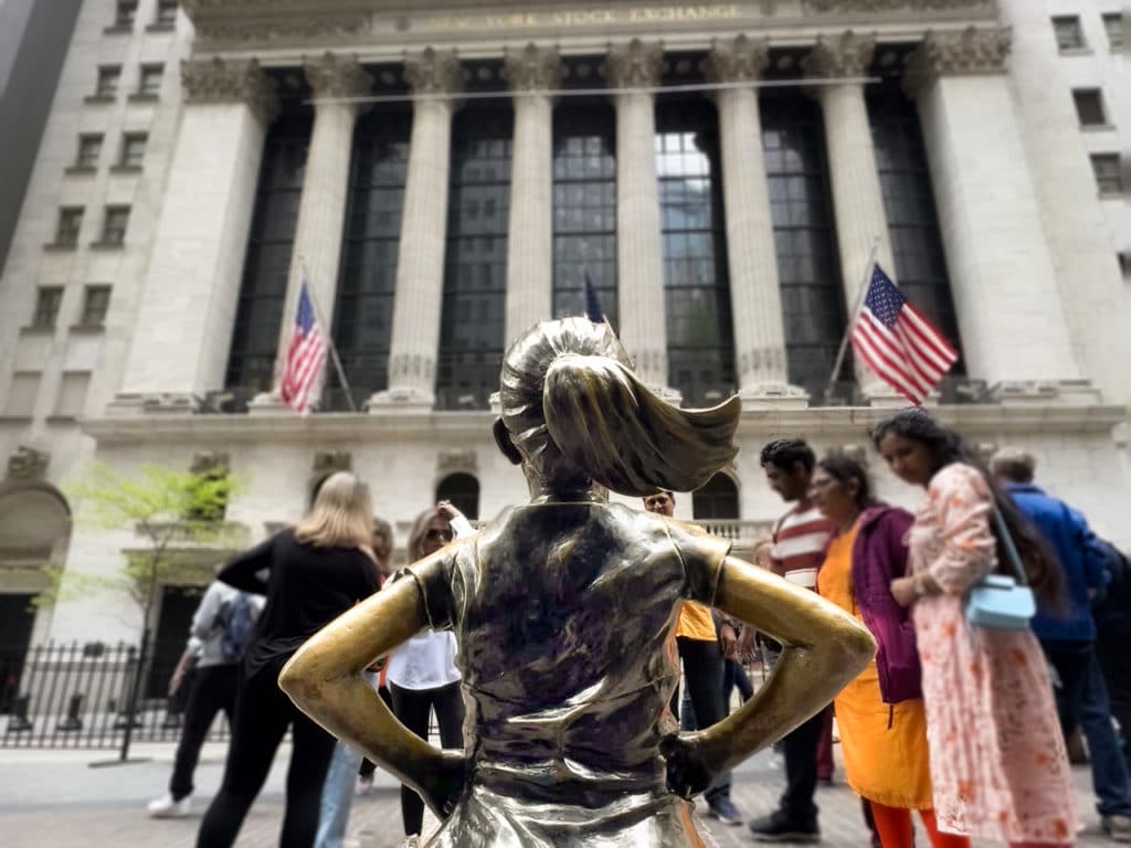 Fearless Girl statue from behind, in front of the New York Stock Exchange.