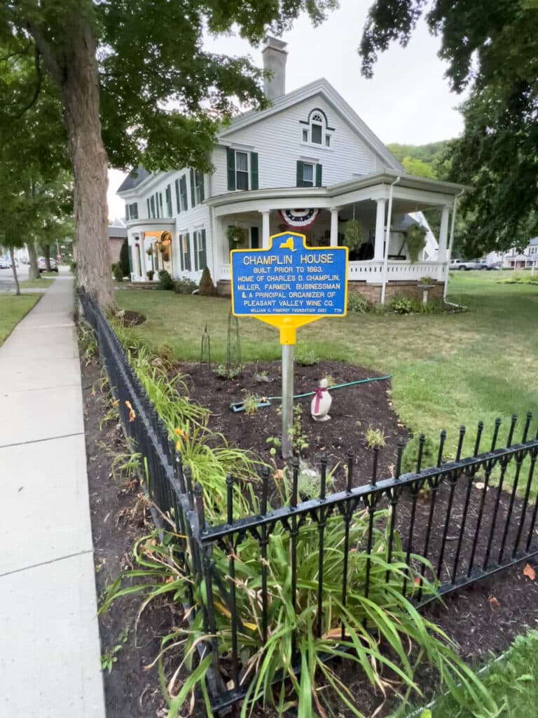 A white, two-story historic house with a blue historical marker in front of it, designating it as Champlin House. 