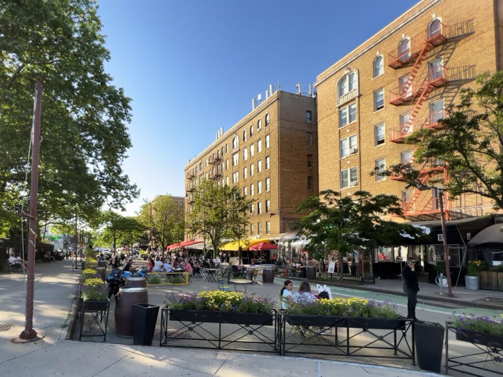 An outdoor pedestrian plaza with cafe tables for dining in the neighborhood of Inwood in New York City.