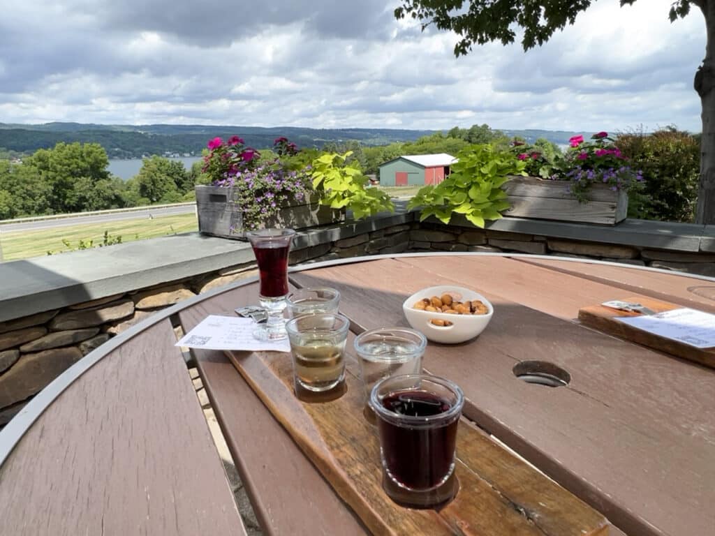 A flight of wines to sample at an outdoor table overlooking a lake. 
