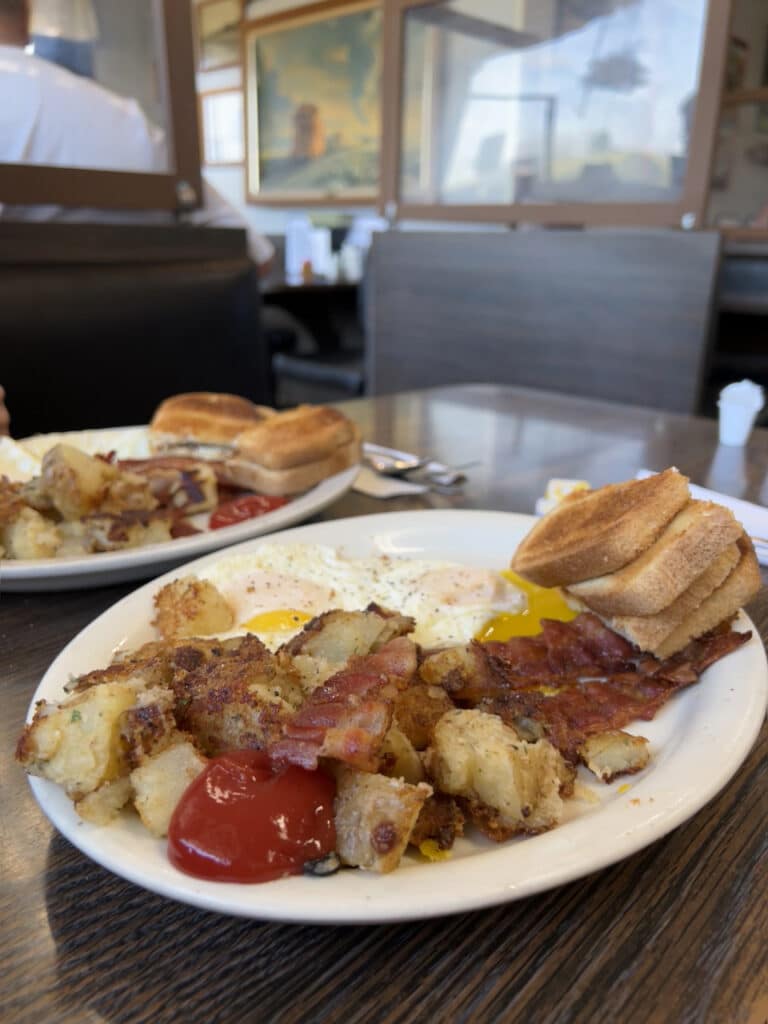 Two plates of fried eggs, bacon, potatoes, and toast. 
