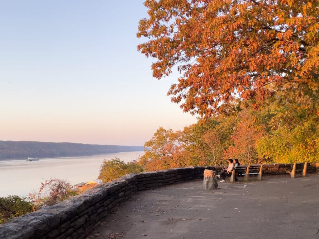 People sitting on a bench overlooking the Hudson River at sunset in Fort Tryon Park, New York City.