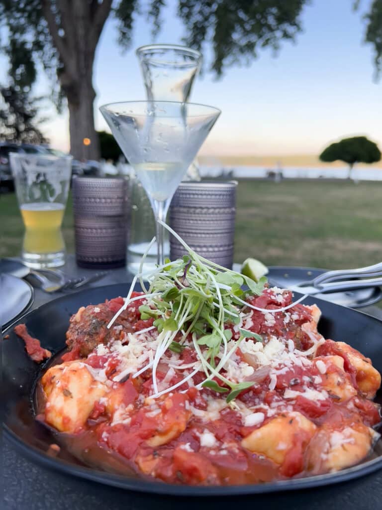 A plate of gnocchi and meatballs covered in red marinara sauce on an outdoor table at a restaurant.