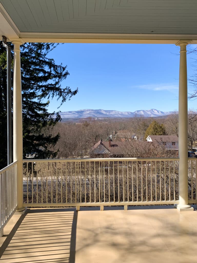 View a mountain range in the distance, framed by the railing of a large porch. 