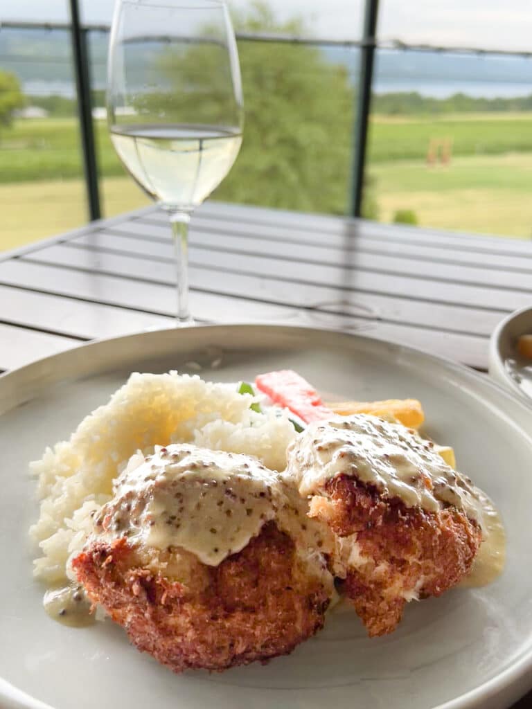 Crab cakes with rice, and a glass of white wine sitting on an outdoor table at a restaurant. 