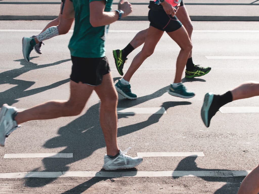 Several people running a marathon. Runners are shown from their torsos to their feet only.