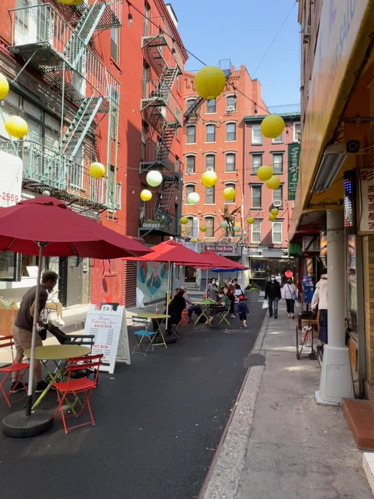 A narrow pedestrian street lined with cafe tables and yellow lanterns strung overhead. 