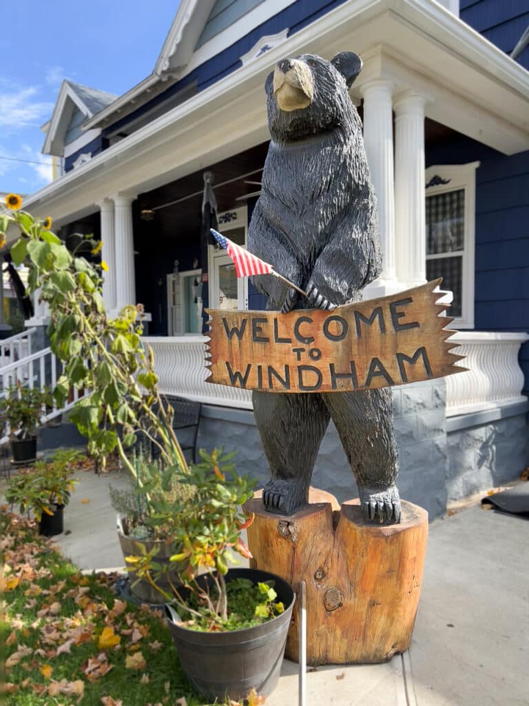 A bear statue holding a wooden sign that says Welcome to Windham. 