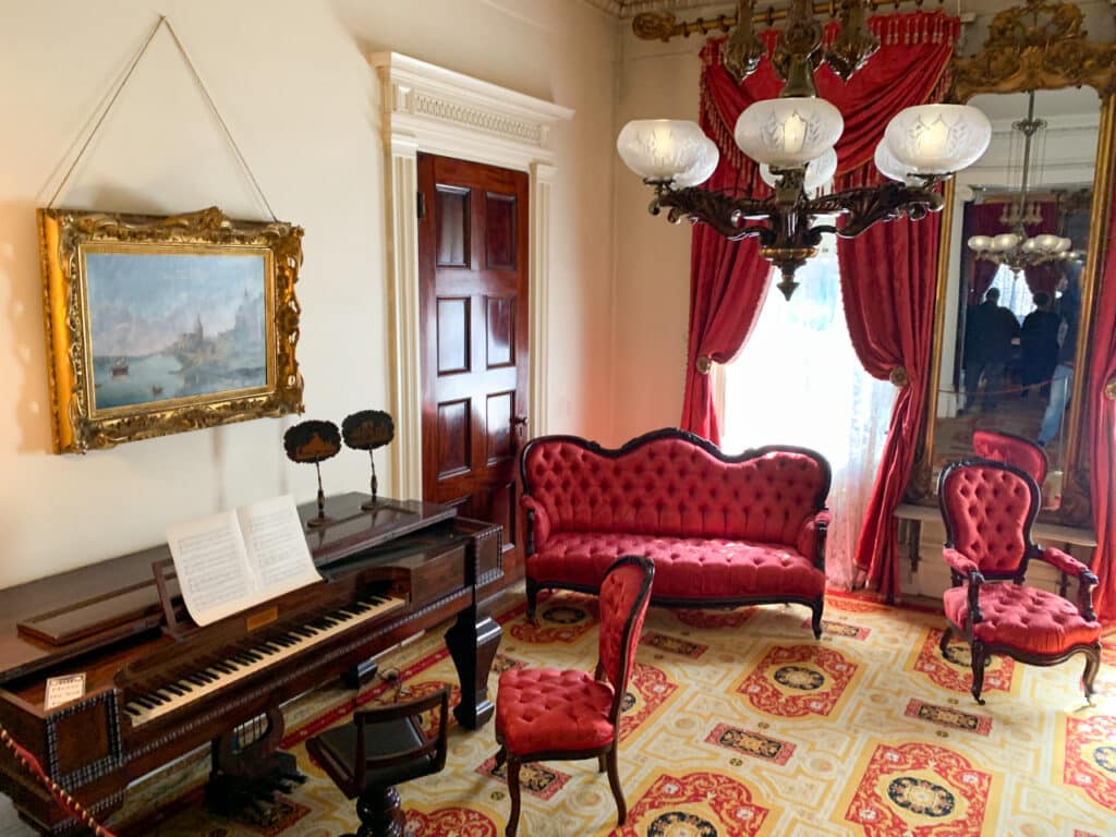 A parlor with red antique furniture and a piano inside the Merchant's House Museum in New York City.
