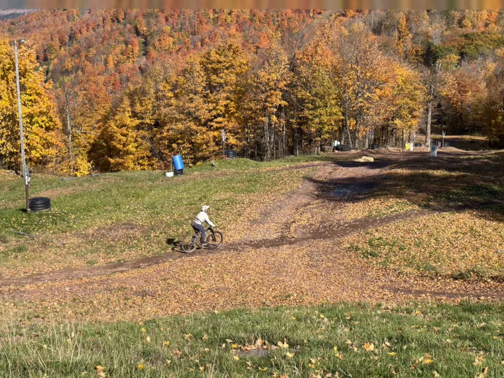 A mountain biker riding on a trail at Windham Mountain, NY, surrounded by fall foliage. 