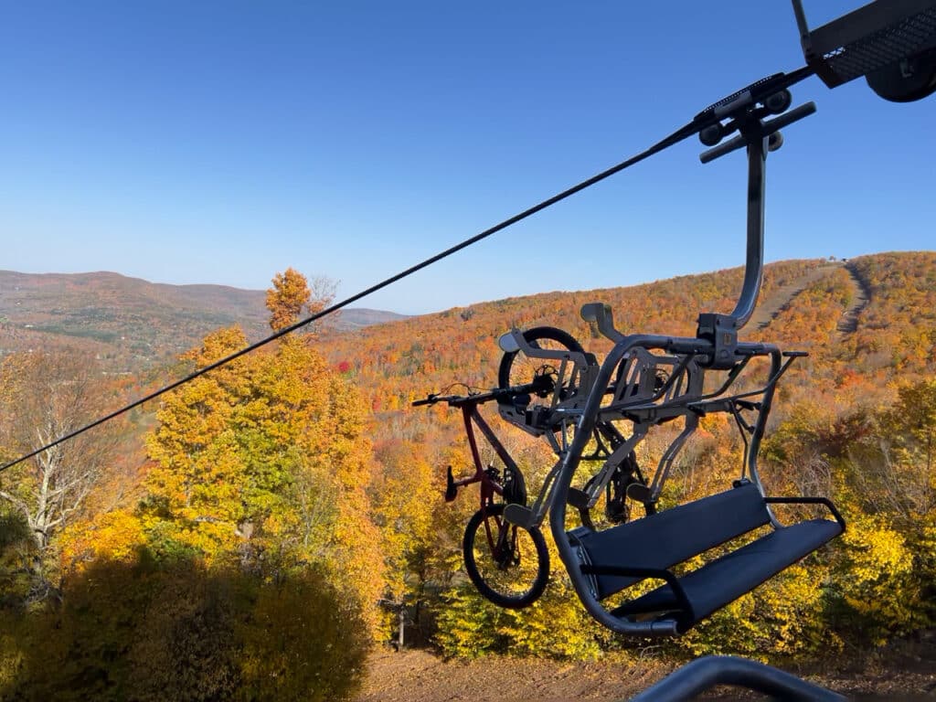 A chair lift carrying a bicycle with colorful fall foliage in the background. 