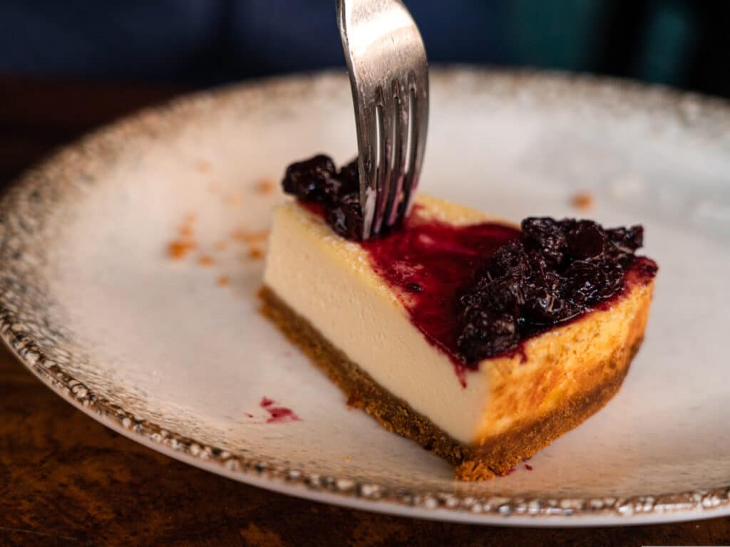 A fork cutting into a piece of cheesecake covered in blueberries. 