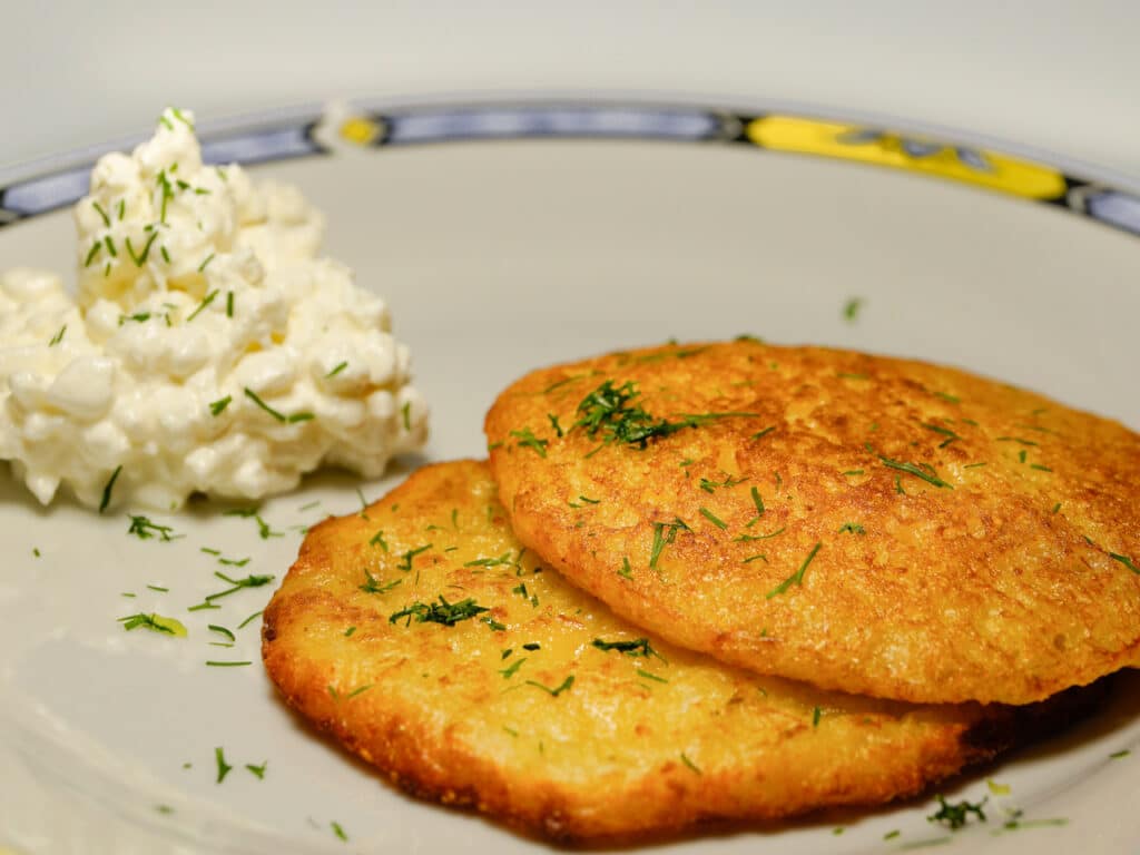 A plate with two latkes and a side of macaroni salad. 