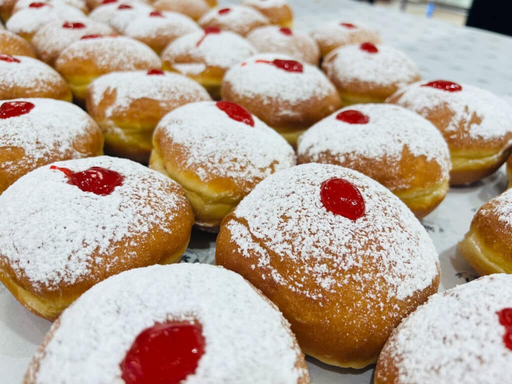 Four rows of jelly-filled doughnuts topped with powdered sugar and a candied cherry each. 