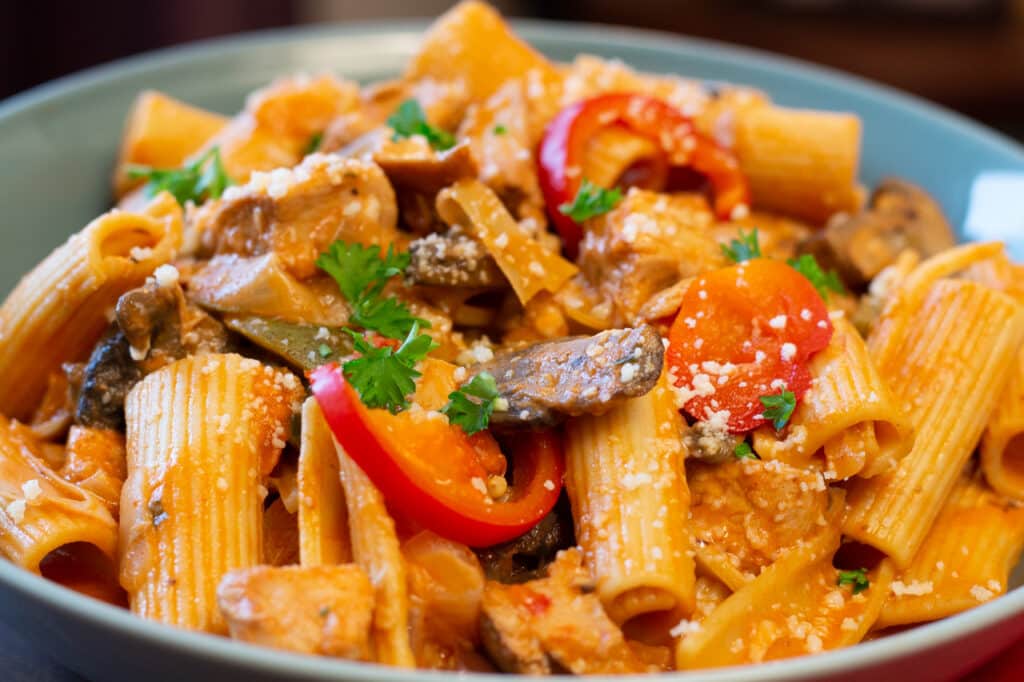 A close-up view of chicken riggies served in shallow, ceramic, blue bowl. 