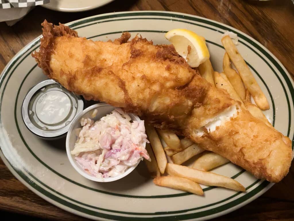 Fried haddock with French fries, coleslaw, tartar sauce, and a lemon slice on the side. 