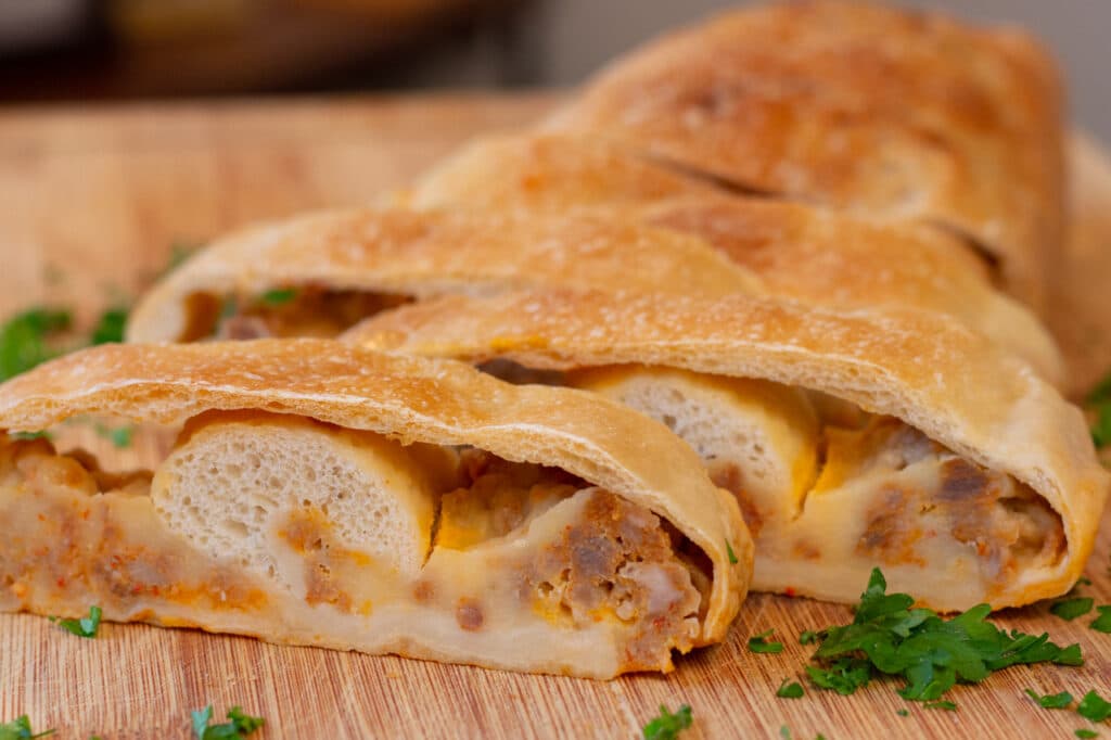 A loaf of sliced Italian sausage roll, sitting on a cutting board and garnished with parsley.