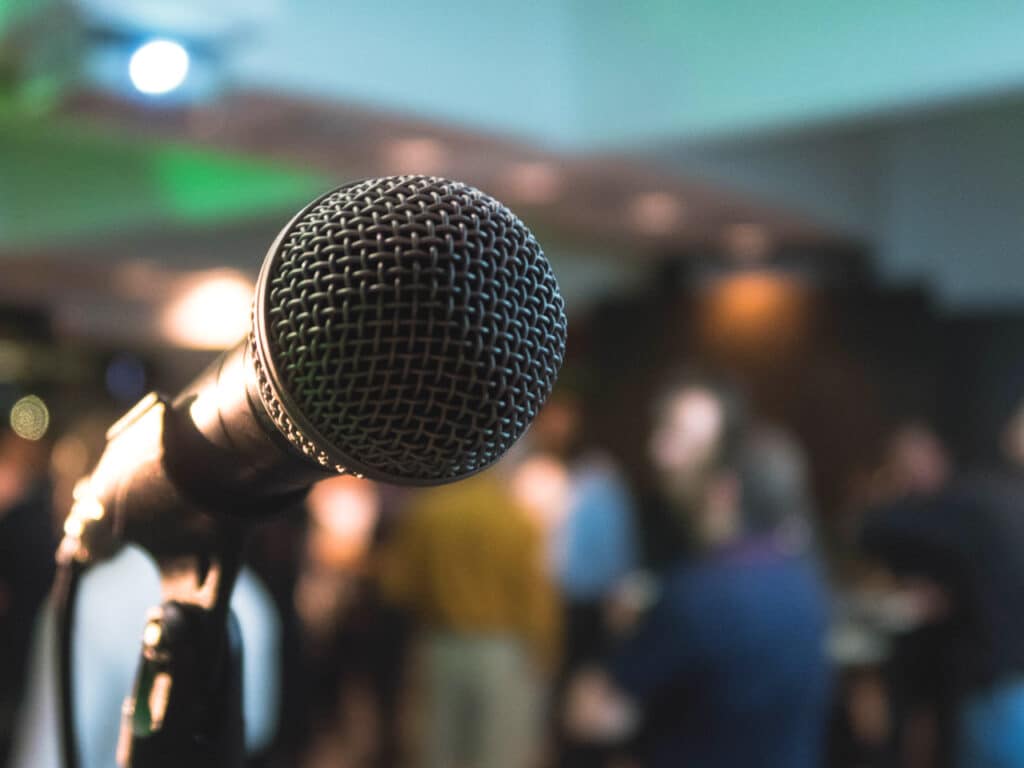 Close-up shot of a microphone with a blurred audience in the background.