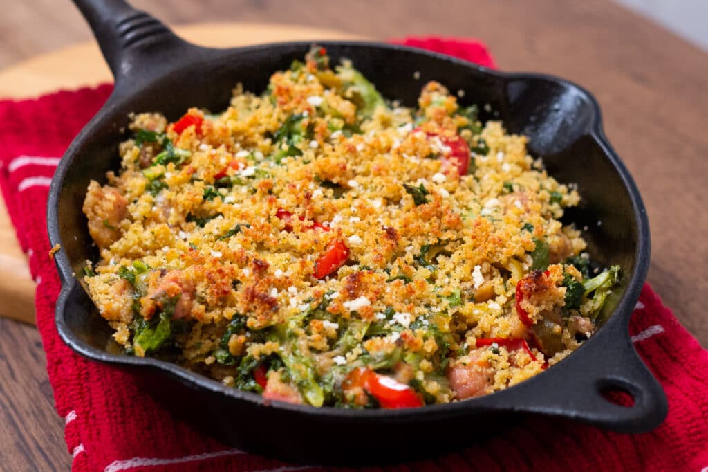 Utica Greens in a cast iron skillet on top of a red and white dish towel. 