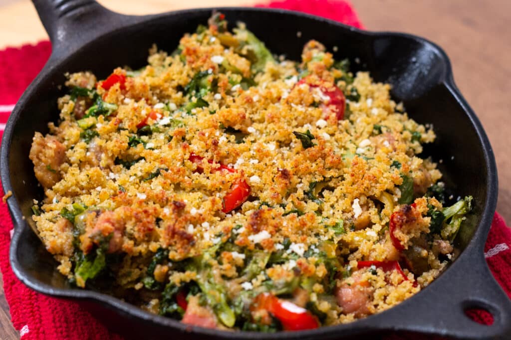 Utica Greens in a cast iron skillet on top of a red and white dish towel. 