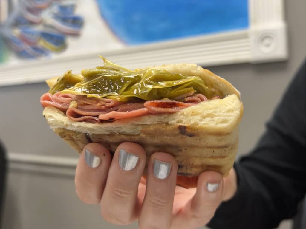 A woman's hand holding fried bologna and hot pepper sandwich.