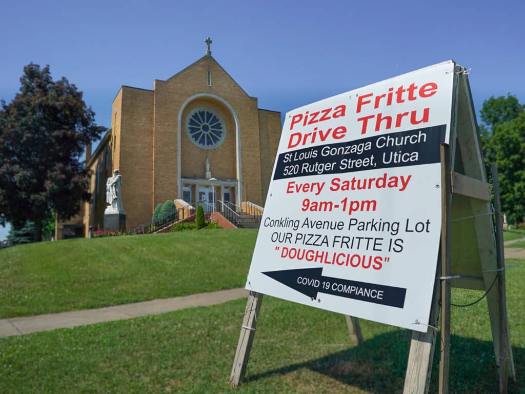 A sandwich board sign that points to a Pizza Fritte Drive Thru. The sign is in front of St. Louis Gonzaga Church in Utica, NY.