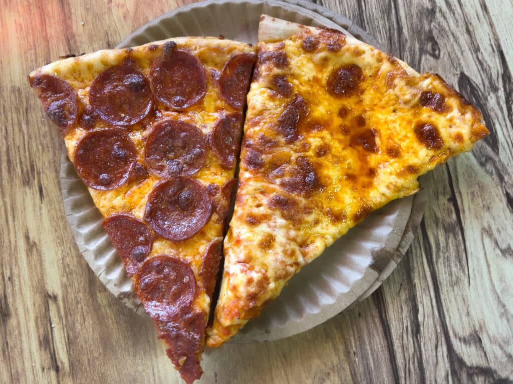 A slice of pepperoni pizza and a slice of cheese pizza on a paper plate. 