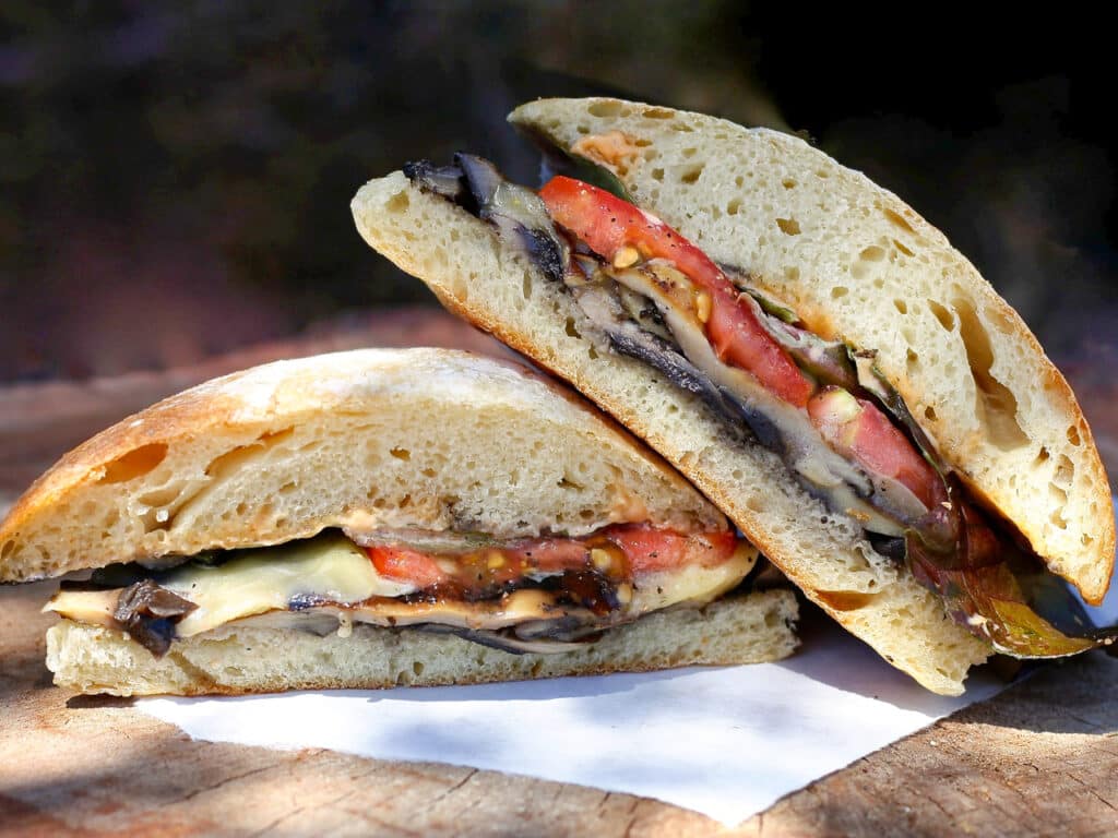 A sandwich, cut in half, made of roasted vegetables and a ciabatta bun. 