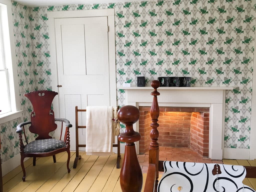 A bedroom with green and white wallpaper and a small brick fireplace. 