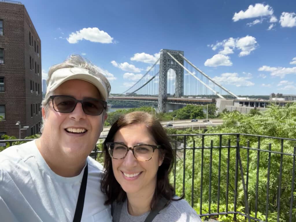A man and woman posing with the George Washington Bridge in the background.