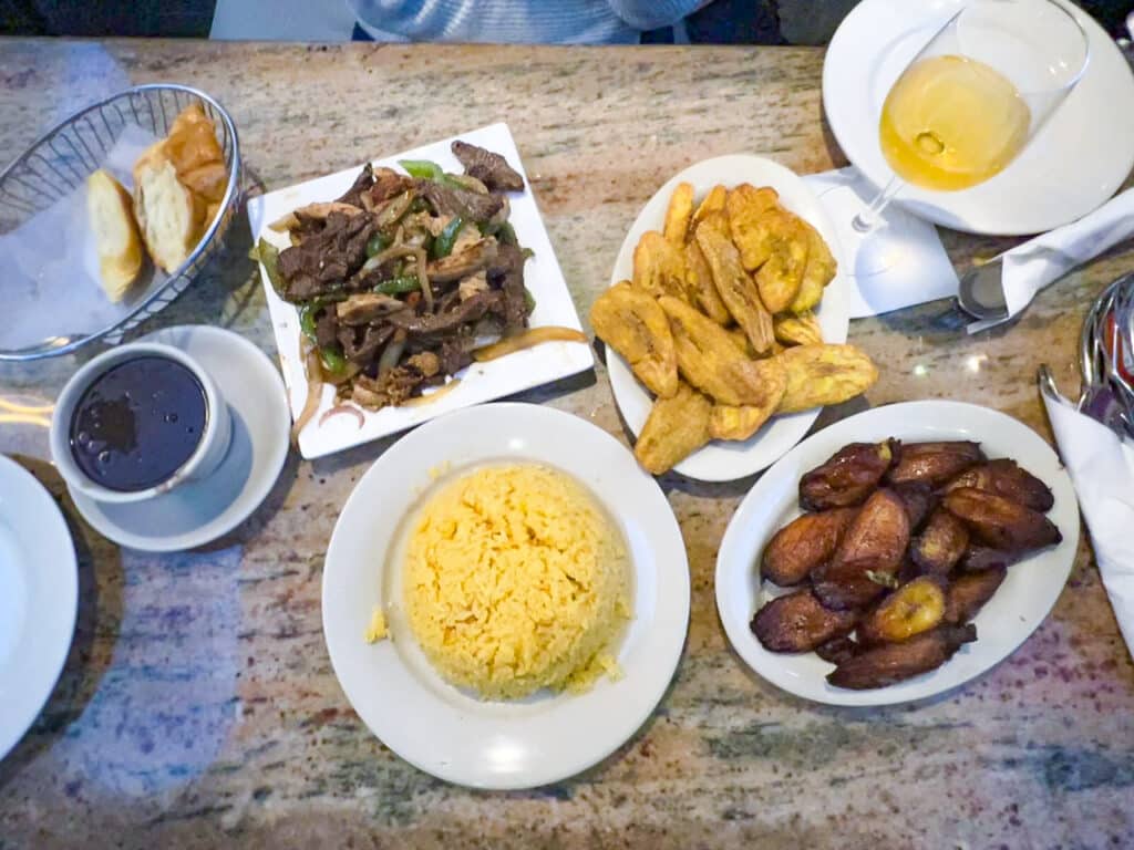 Beef and peppers, rice, plantains, and black beans laid out on a restaurant table.