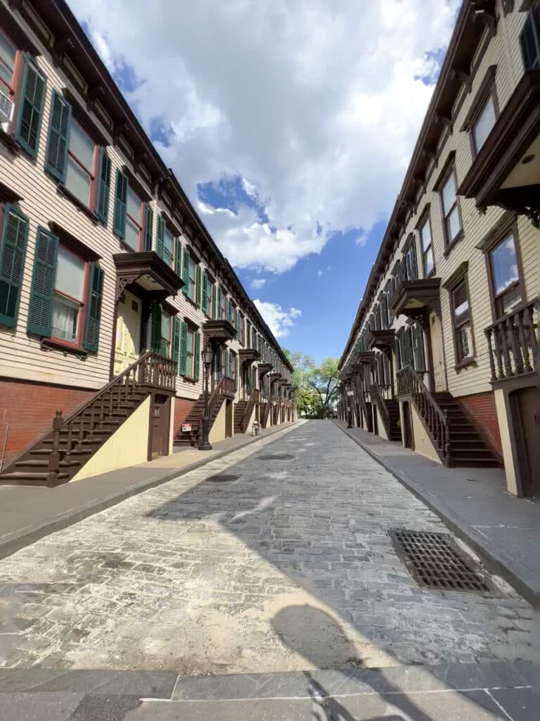 A one-block long brick street lined with identical yellow and brown row houses. 